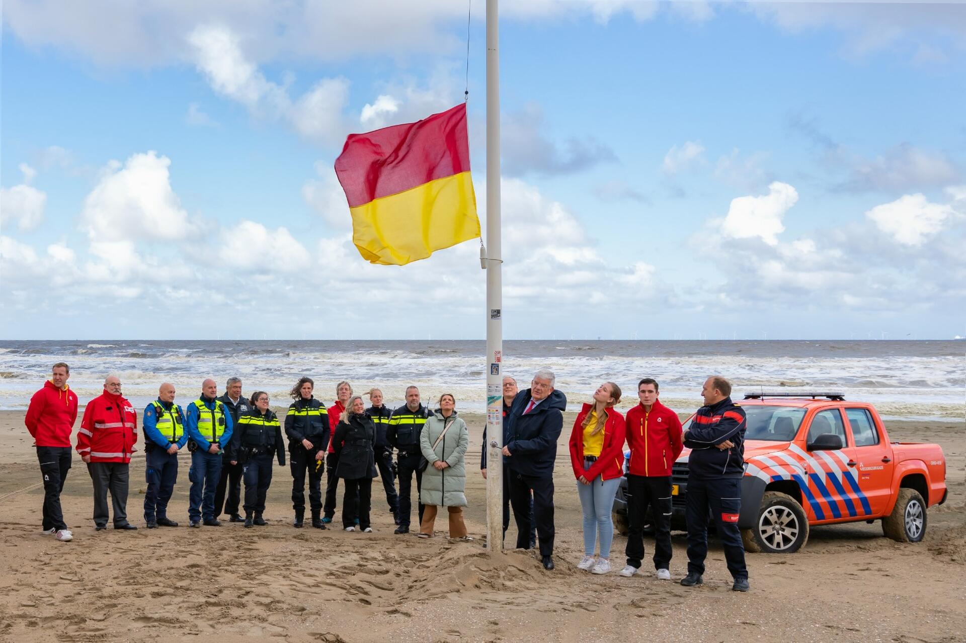 De rood gele vlag is gehesen. Eromheen staat de burgemeester samen met lifeguards, brandweer- en politiecollega's 