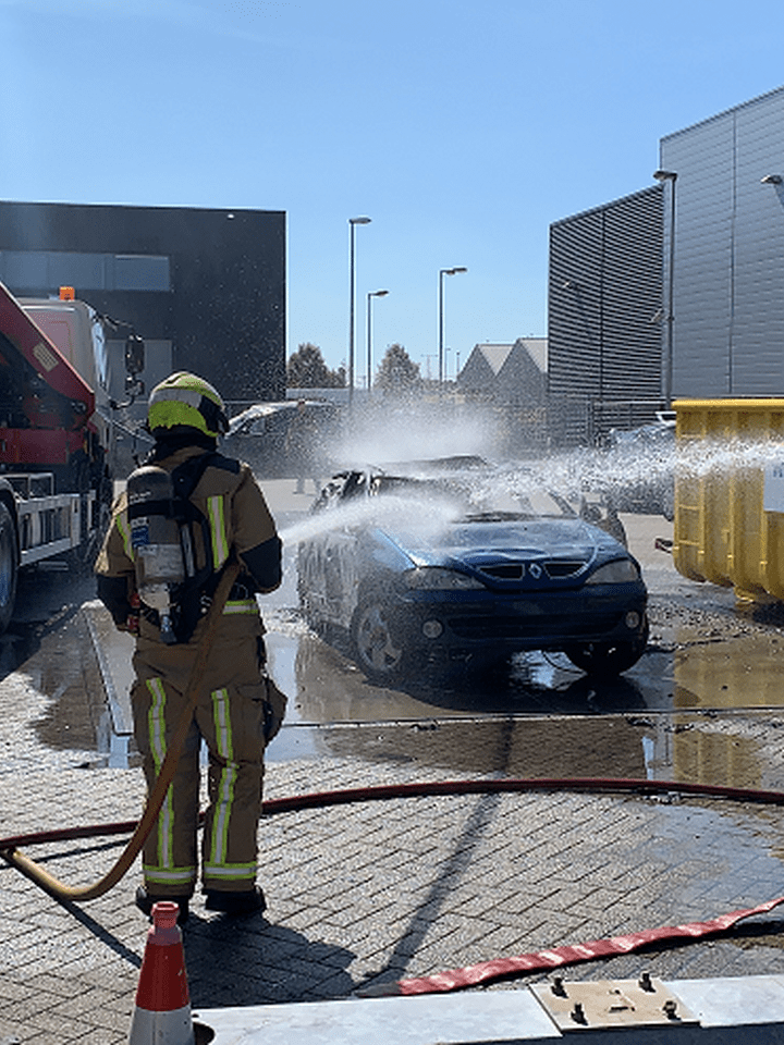 Brandweermannen blussen een auto op oefenterrein