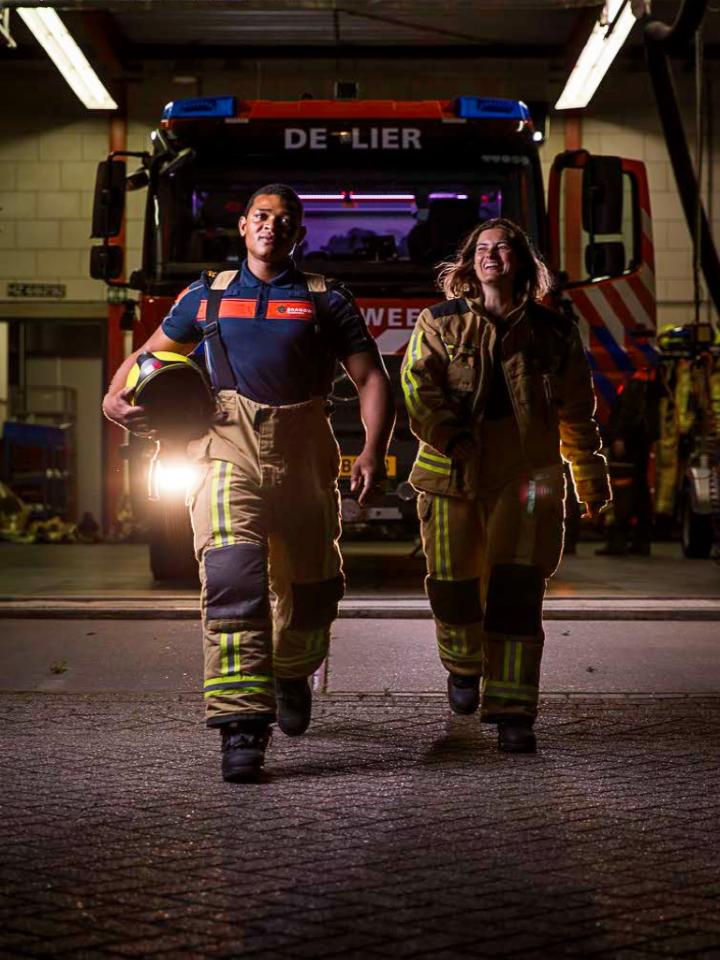 Vrijwilligers brandweer lopen in bluspak richting camera