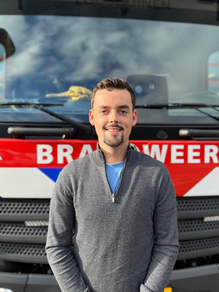 Jongen man met een grijze sweater voor een brandweerwagen