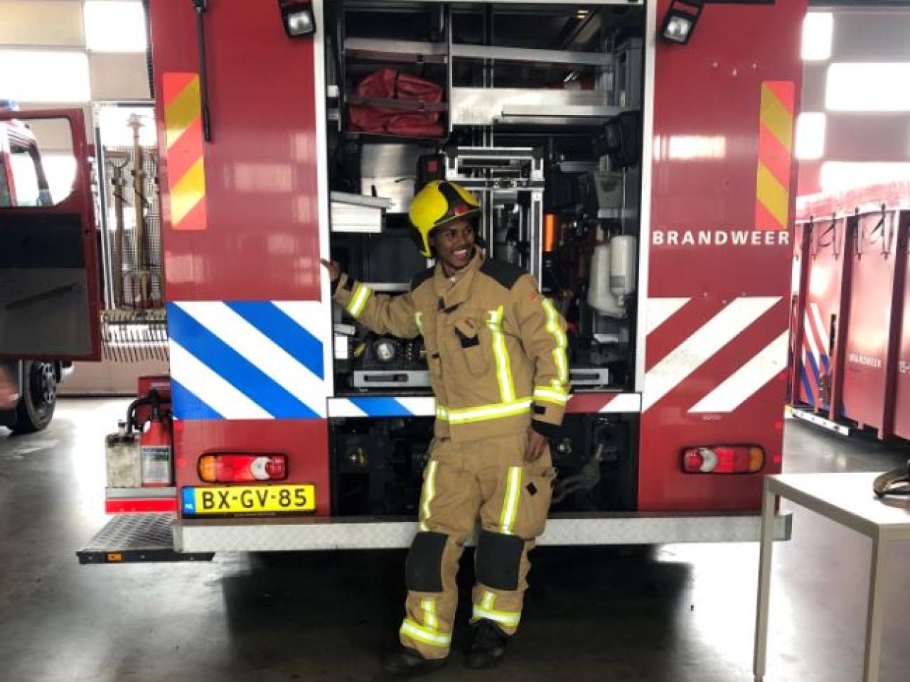 Inburgeraar gekleed als brandweerman poseert voor brandweerwagen
