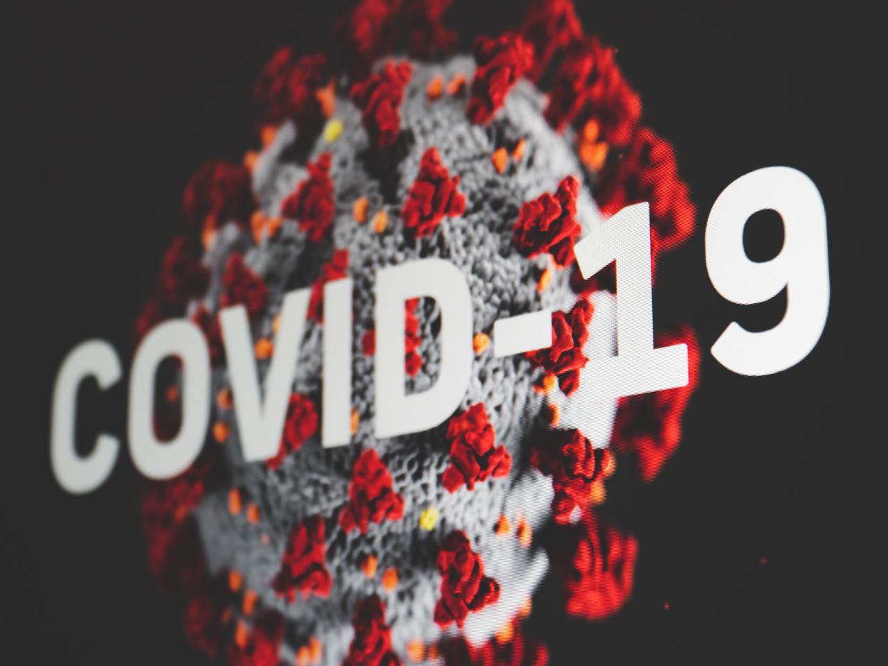 Microscopische weergave van het coronavirus, daaroverheen de tekst Covid-19