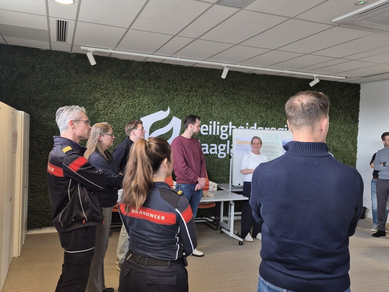 Een foto met mensen van verschillende organisaties die voor een whiteboard staan en met elkaar praten.