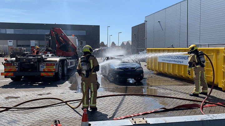 Brandweermannen blussen een auto op oefenterrein