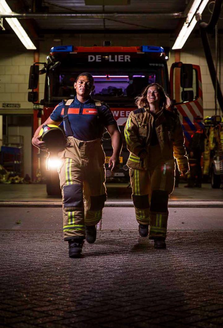Vrijwilligers brandweer lopen in bluspak richting camera