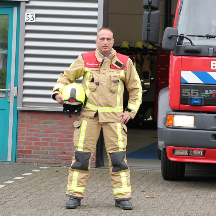 Bevelvoerder John poseert met helm bij brandweerwagen