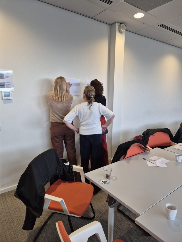 Een foto met mensen van verschillende organisaties die staan te schrijven op een vel papier.